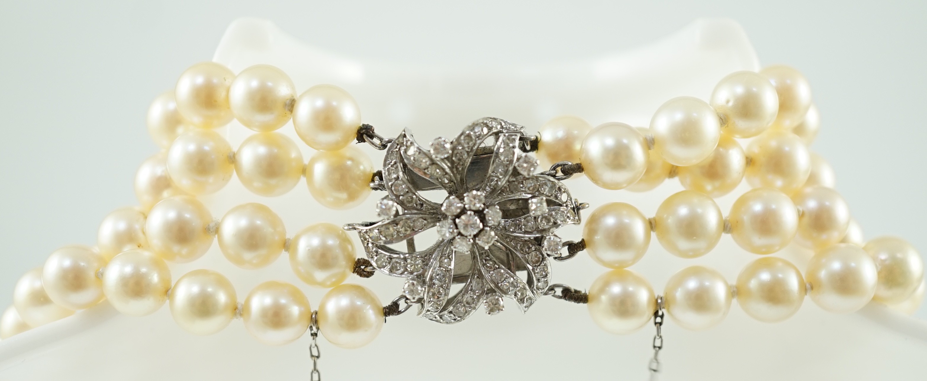 A mid to late 20th century continental quadruple strand cultured pearl necklace, with white gold and diamond cluster set flower head clasp